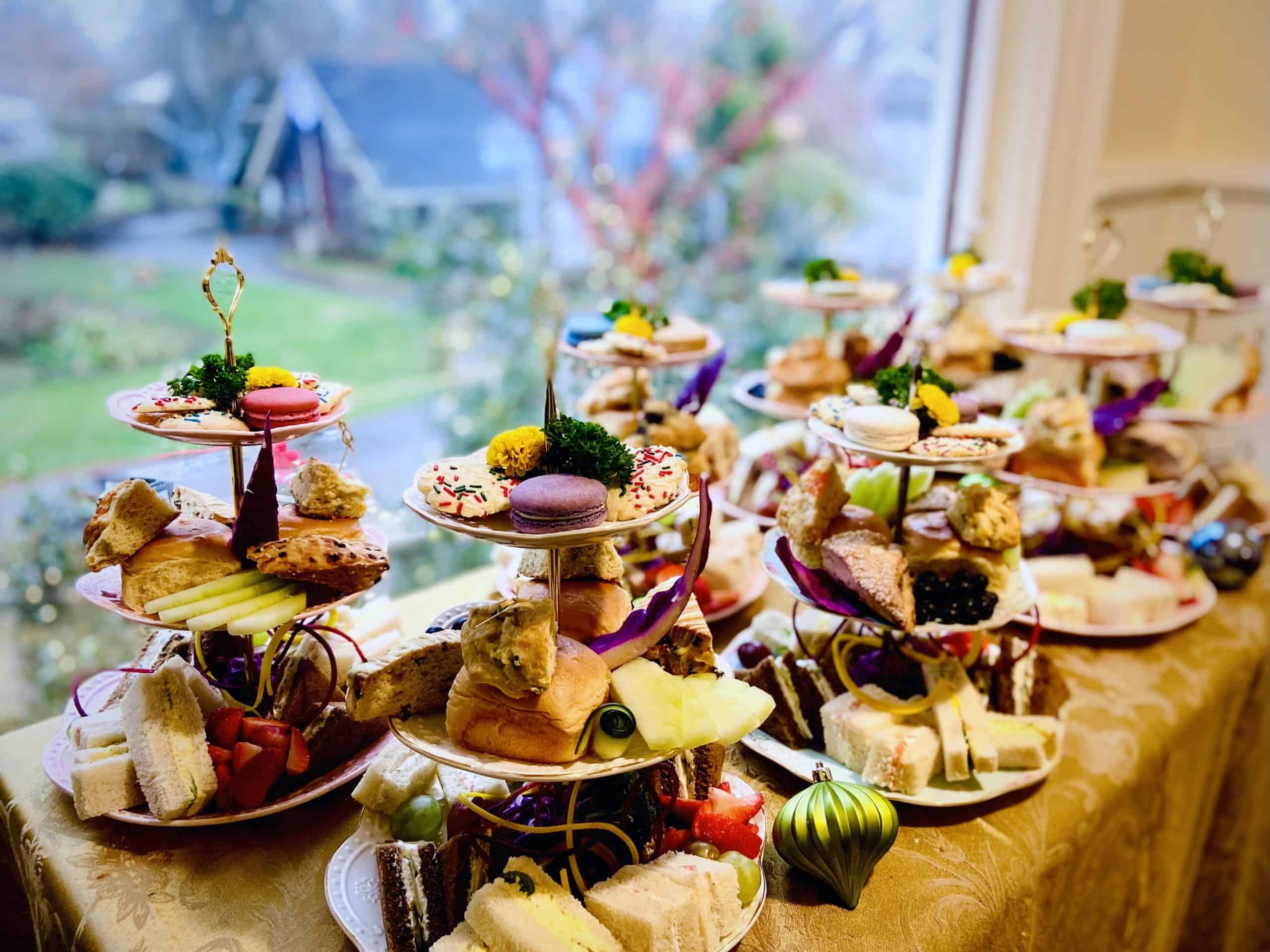 Tea sandwiches, scones, fruit, and pastries rest on three-tiered plates in front of a window