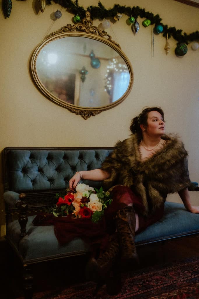 A bride sits on a velvet sofa wearing a fur wrap