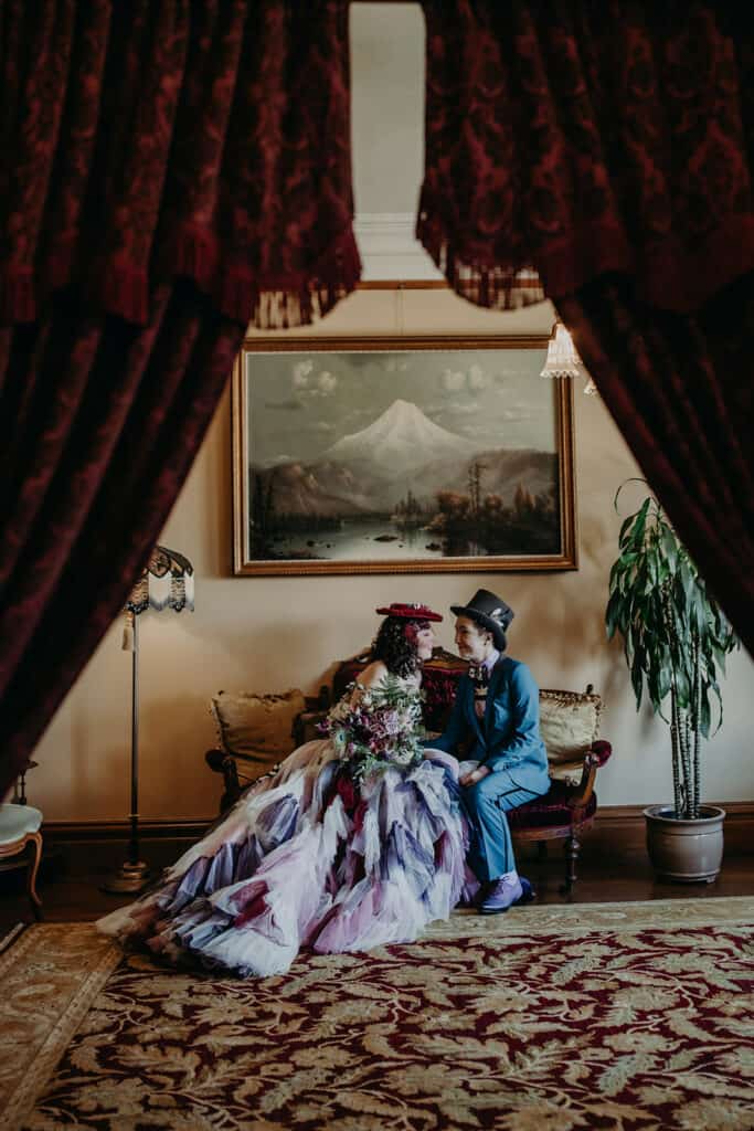 A couple sits on an antique sofa under a painting of Mount Hood.