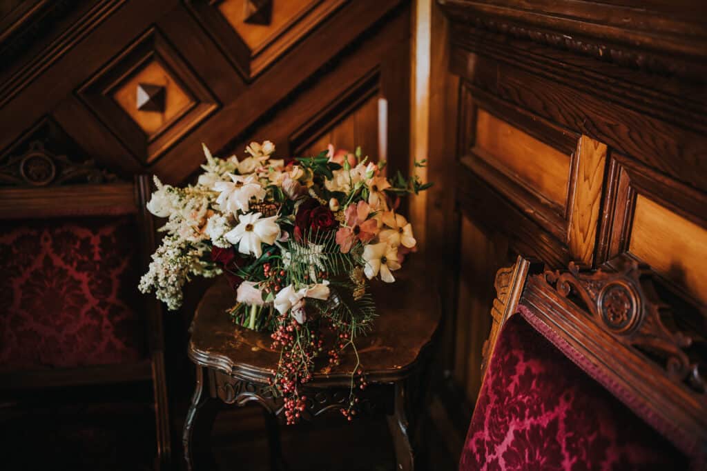 A bouquet of flowers sits on an antique table in front of ornate woodwork.