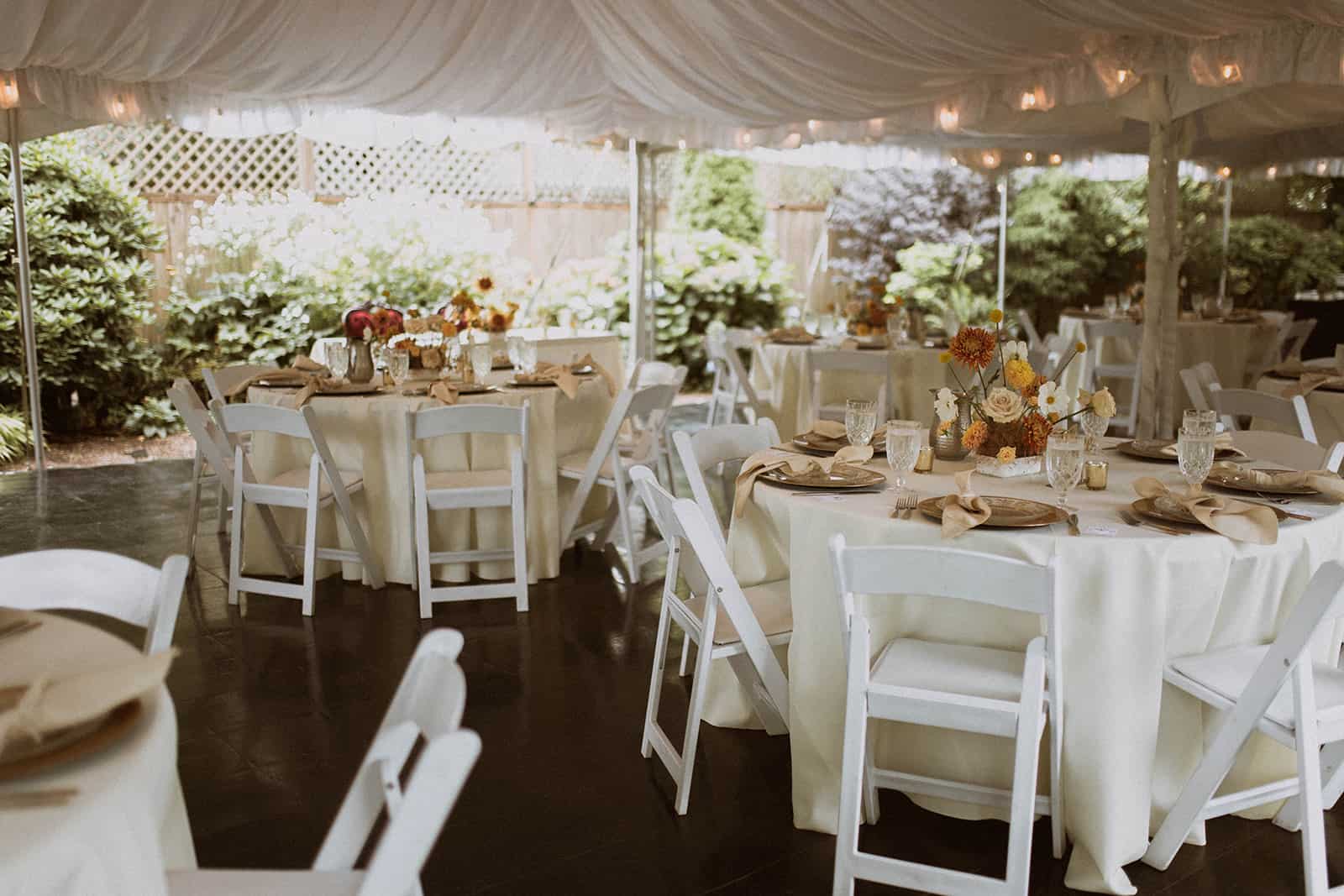 A dining tent set with round tables, chairs, and place settings with floral centerpieces.